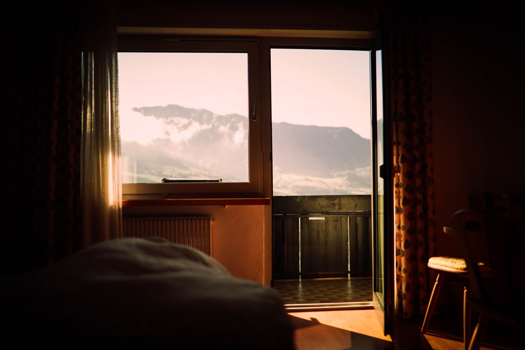 Camera al tramonto con la portafinestra sul balcone e le cime
