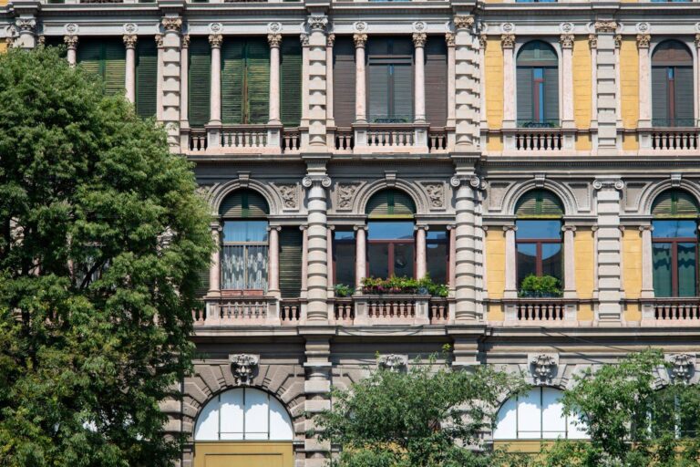 La facciata di un palazzo d’epoca con i balconi in pietra e gli alberi davanti