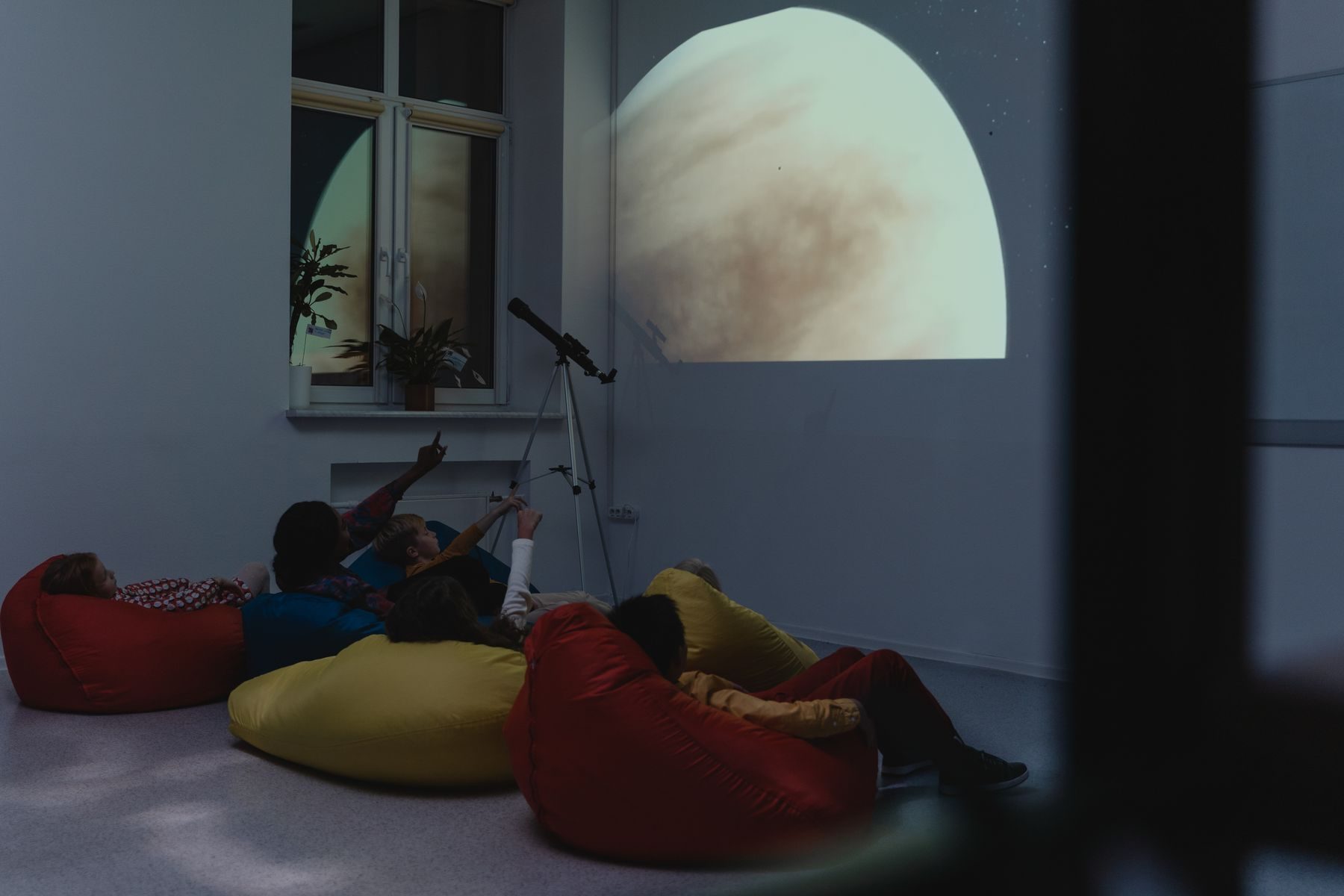 Bambini sdraiati sui pouf guardano la Luna proiettata sul muro