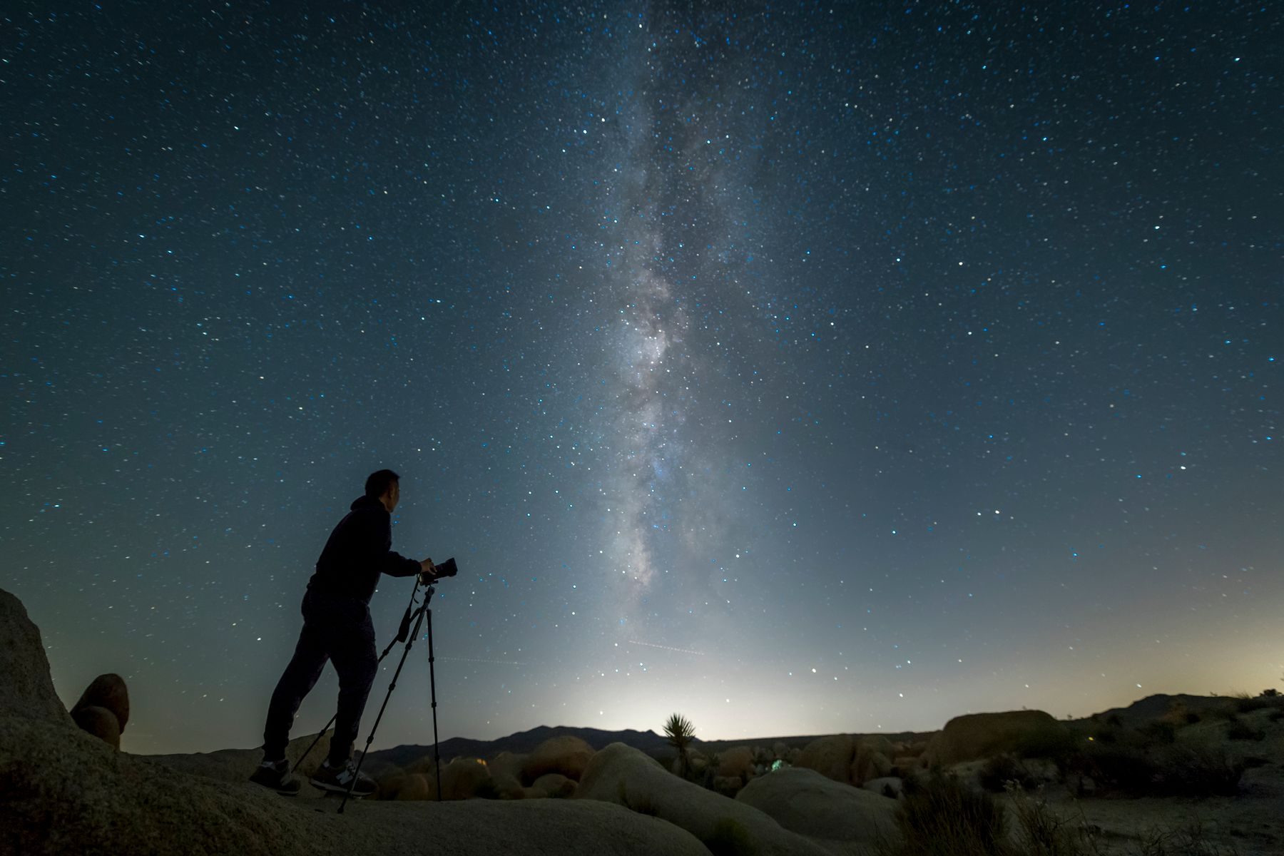 Una persona accanto a un telescopio, controluce sotto la Via Lattea