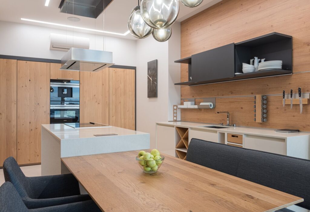Una cucina in legno con l’isola e il tavolo, sotto le lampade di vetro