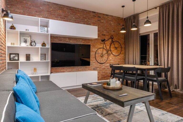Un soggiorno con i cuscini blu, la libreria bianca e una bicicletta appesa ai mattoni