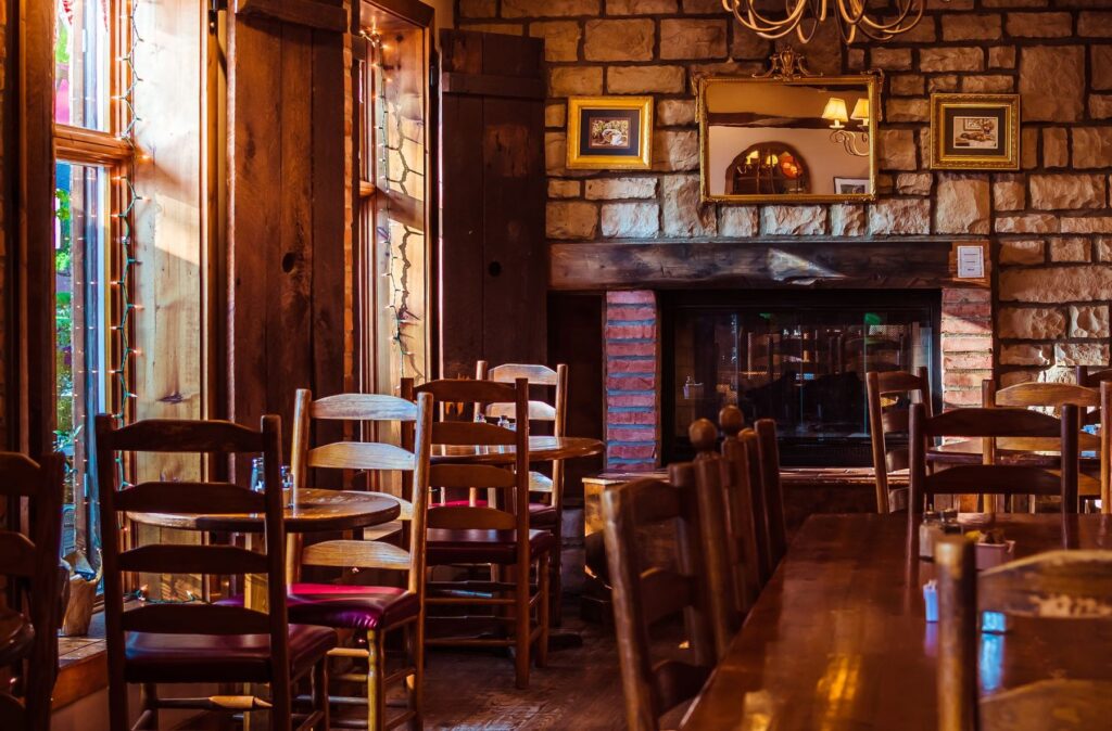 Una sala di pietra col camino, le sedie di legno e le luci basse