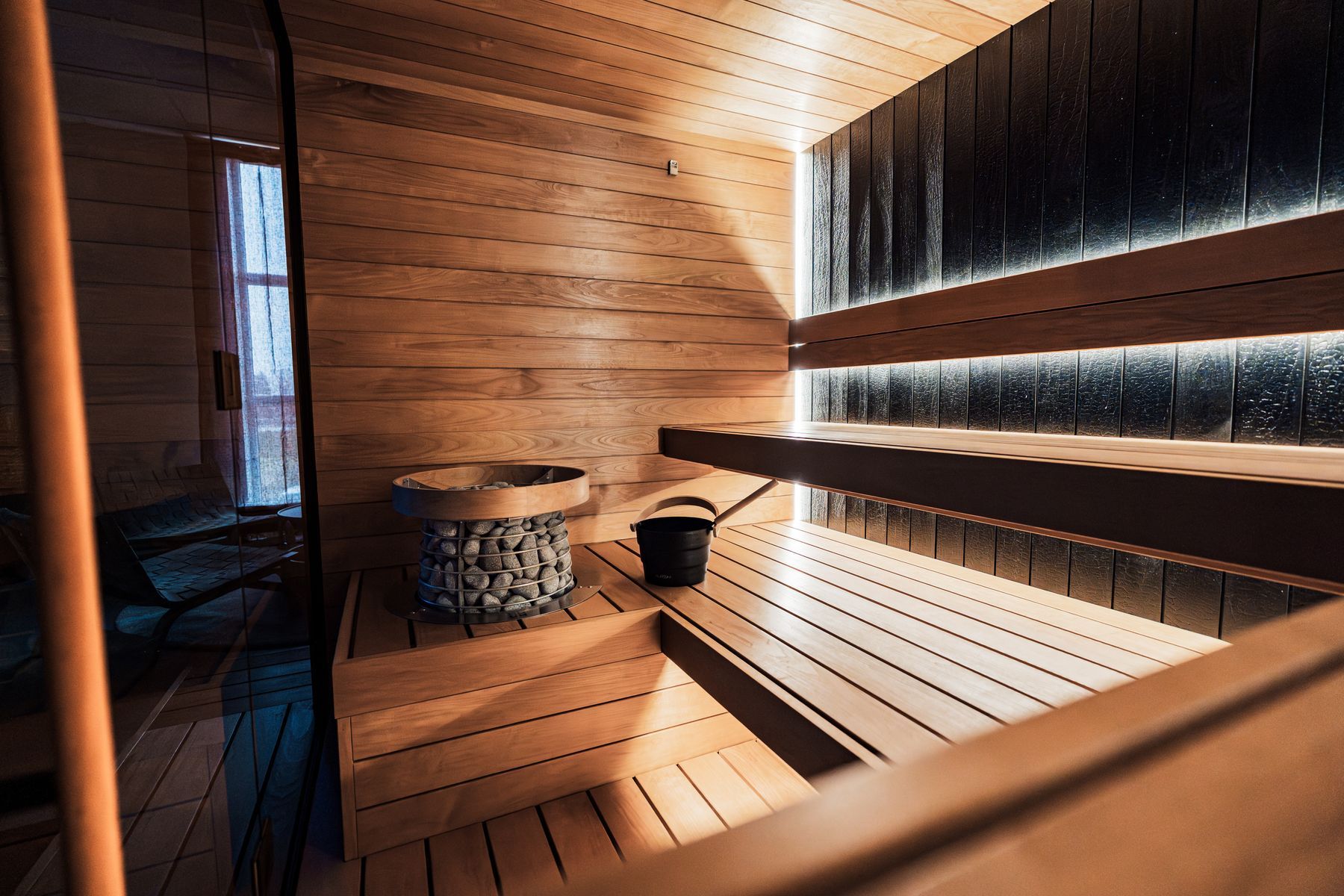 La sauna con la stufa a pietre, il secchio nero e la luce sotto le panche