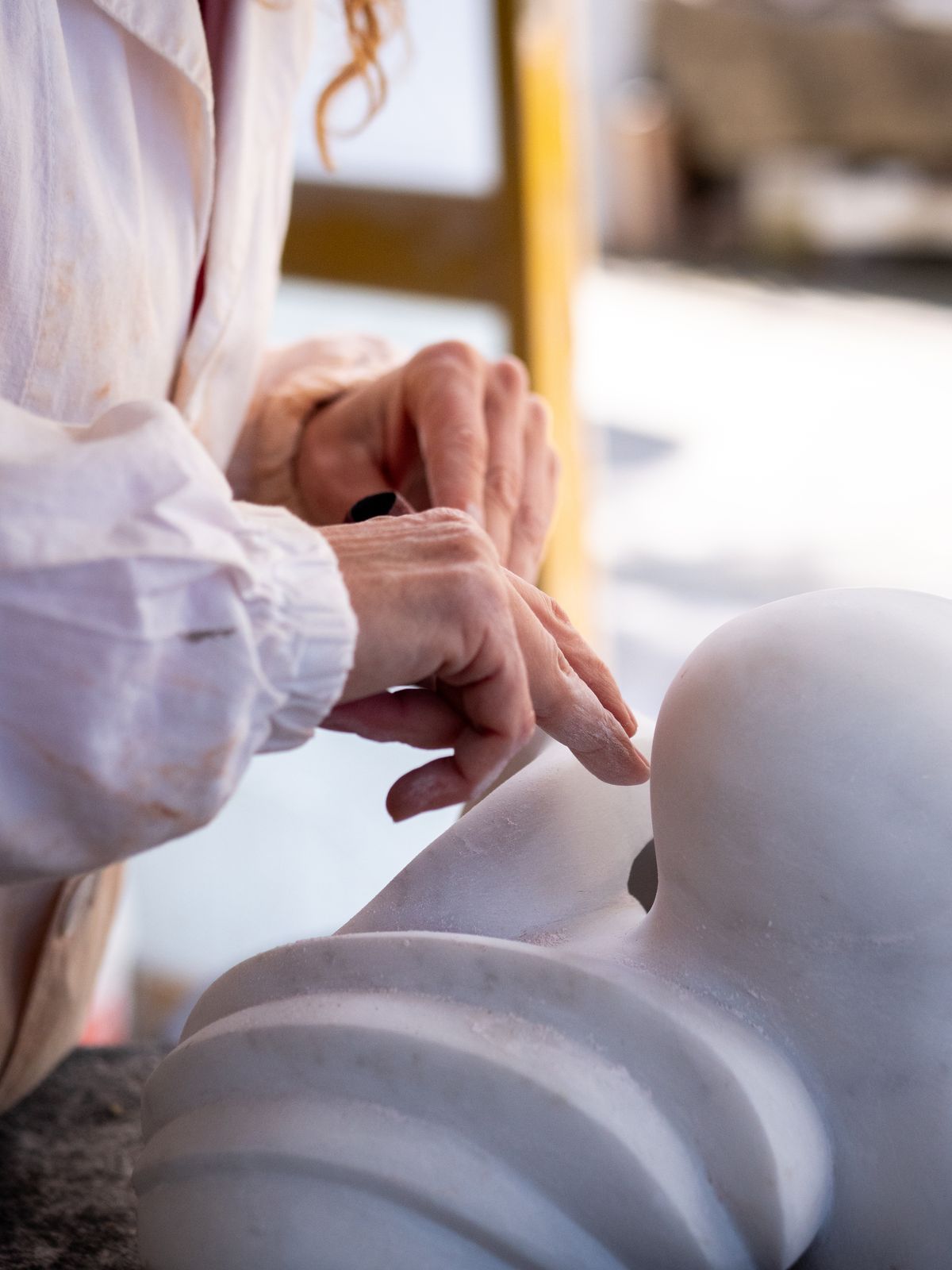 Le mani di uno scultore rifiniscono una forma morbida in marmo bianco
