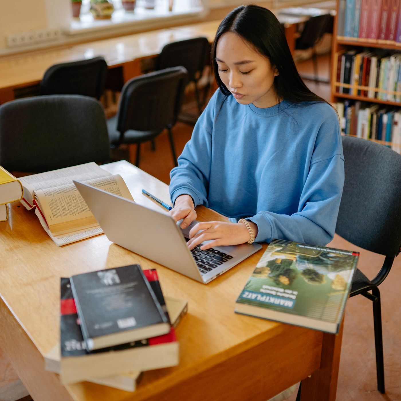 Una ragazza al computer fra i libri della biblioteca