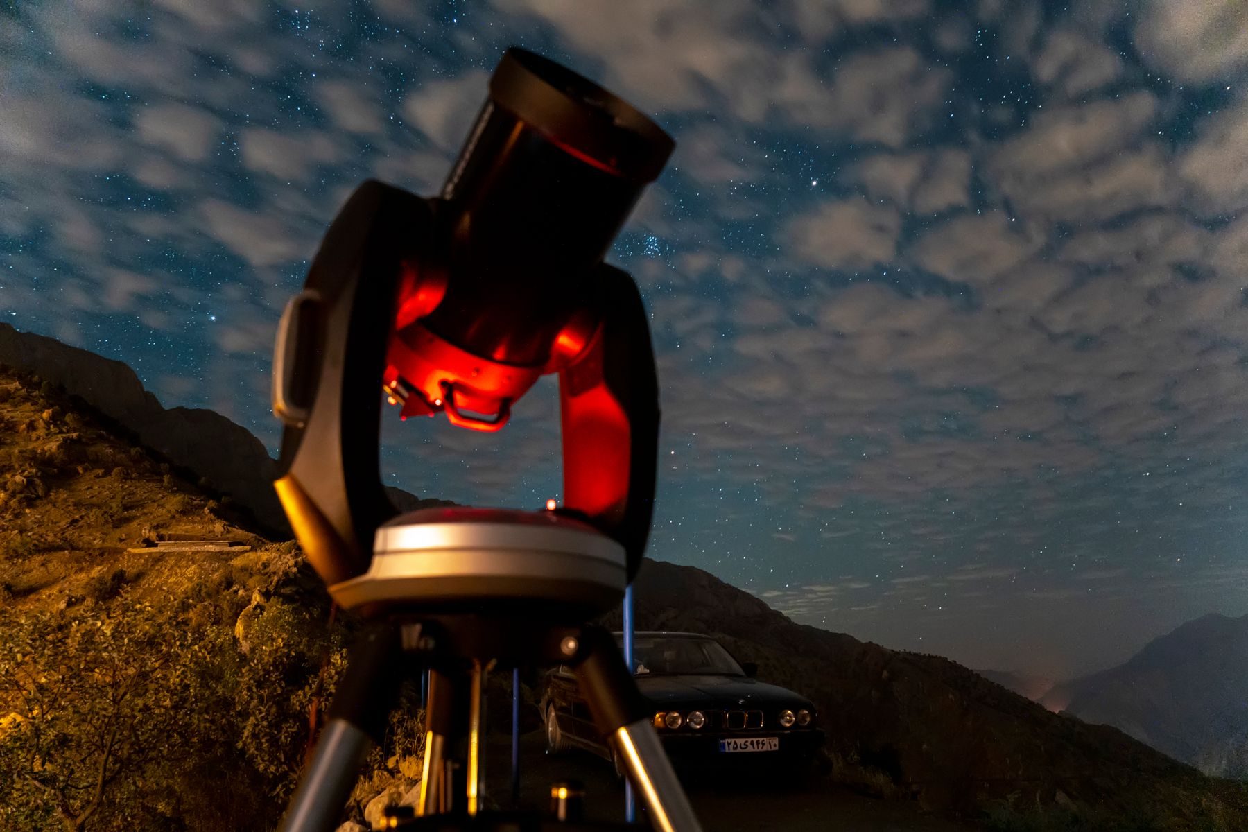 Un telescopio rosso puntato verso un cielo con le nuvole e le stelle