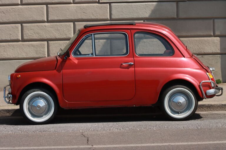 Una Fiat 500 d’epoca rossa, di profilo, davanti a un muro