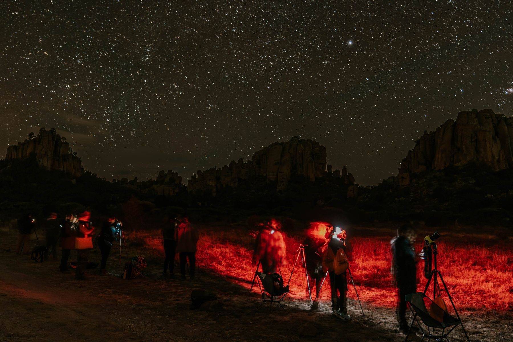 Persone con le torce rosse attorno ai telescopi, sotto un cielo pieno di stelle