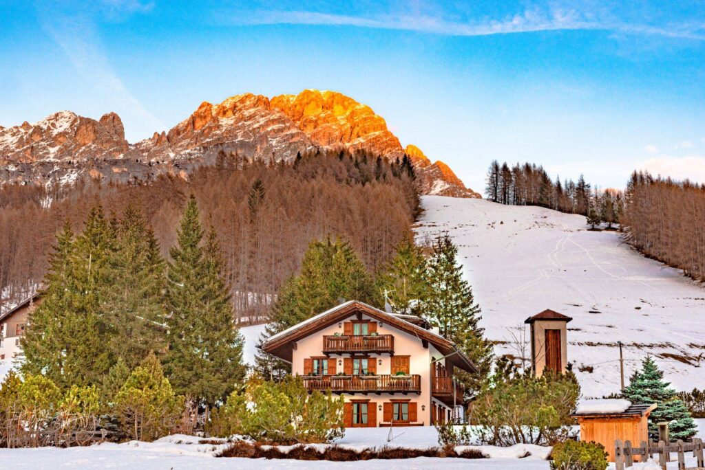 Grande baita di legno con i balconi, nella neve, sotto le cime accese dal tramonto