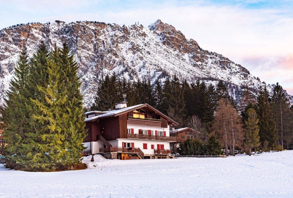Casa di legno con le imposte rosse nella neve, sotto la montagna