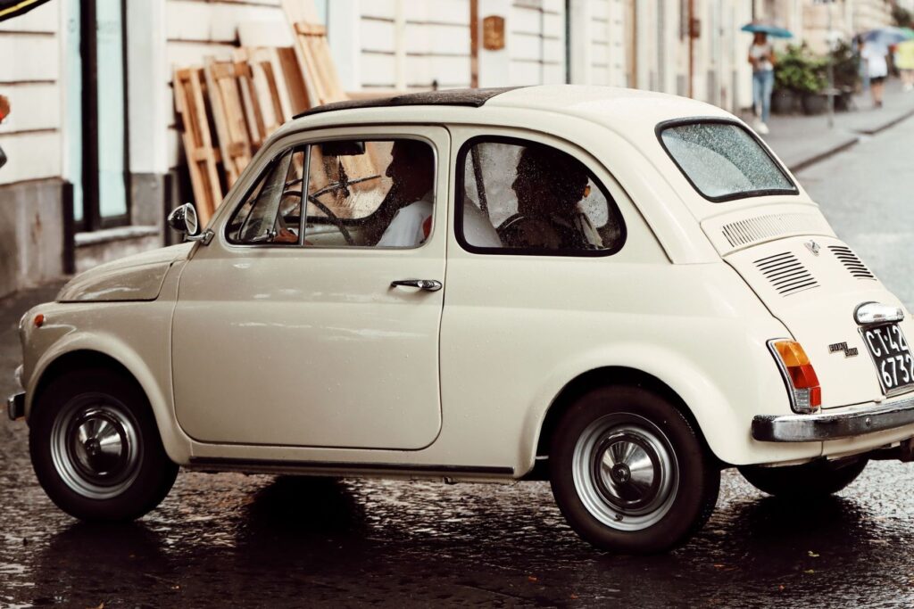 Una Fiat 500 d’epoca color crema, ferma in una piazza