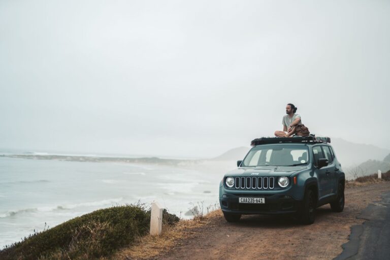 Una Jeep Renegade verde ferma su un promontorio sopra il mare, con una ragazza sul tetto