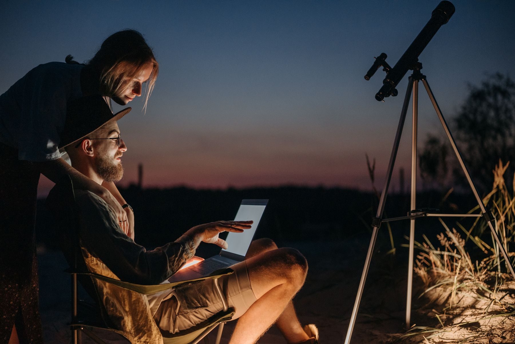Una coppia controlla una mappa del cielo sul tablet accanto al telescopio, al tramonto